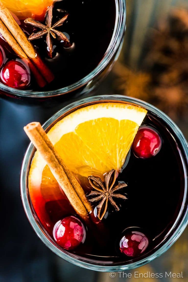A close up of a glass of mulled wine with an orange slice, cinnamon stick, and a few cranberries in it. 