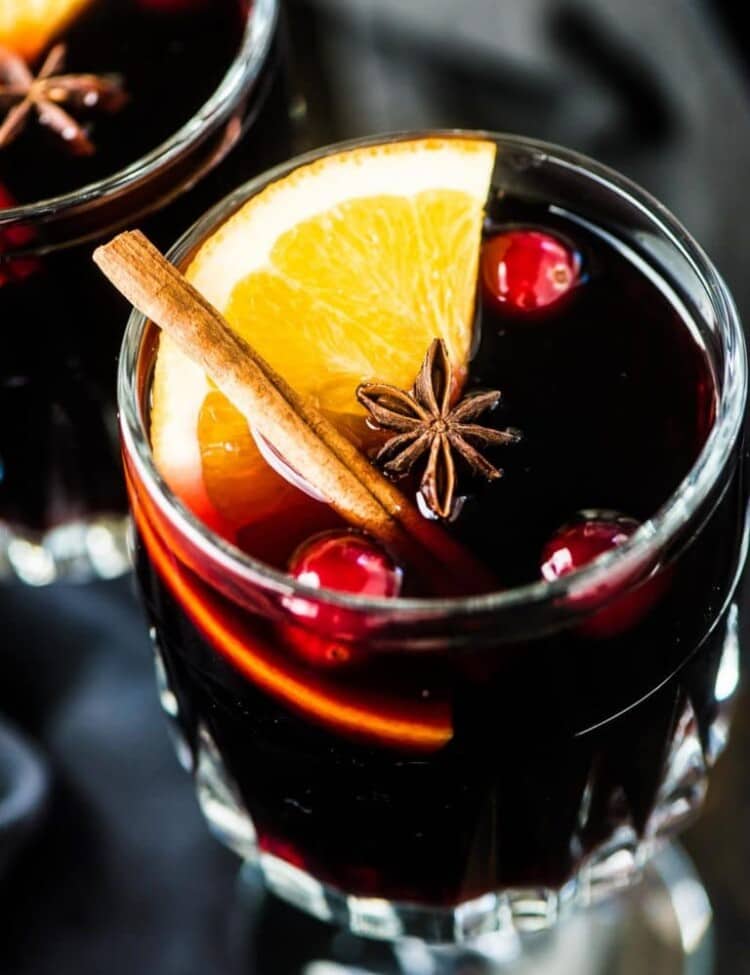 A glass of mulled wine with an orange slice, cinnamon stick, and a few cranberries in it.