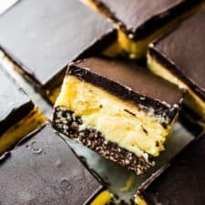 A close up of classic Canadian Nanaimo bars with one on its side so you can see the yellow custard.