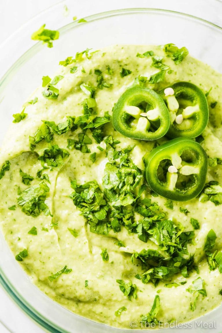 Creamy Avocado Sauce in a glass bowl with minced cilantro and sliced of jalapeño peppers on top. 