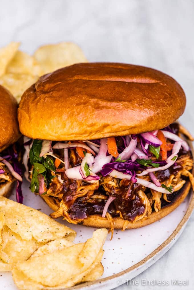 A pulled chicken sandwich on a plate with potato chips.