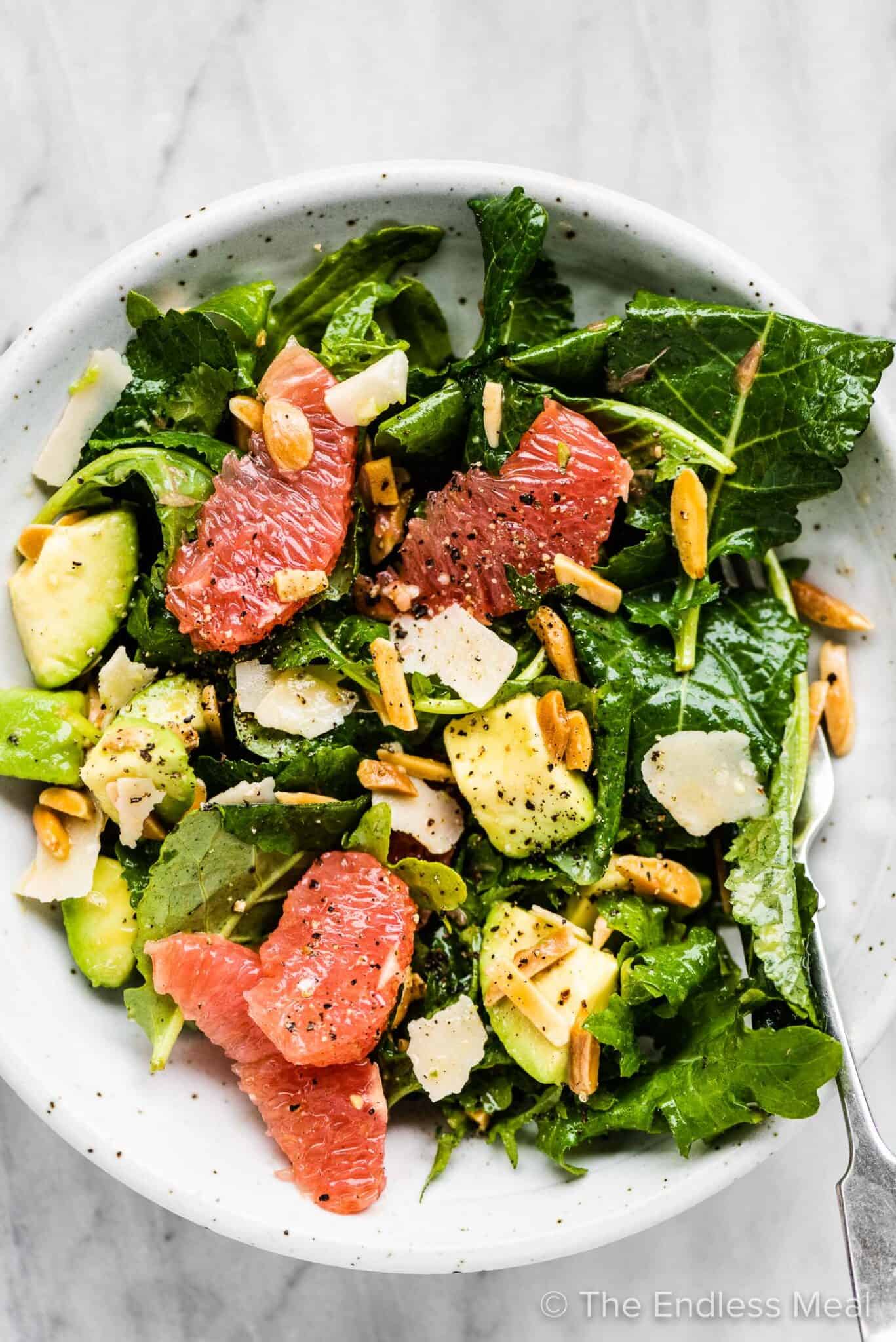 Baby kale salad on a plate with grapefruit, avocados, and almonds.