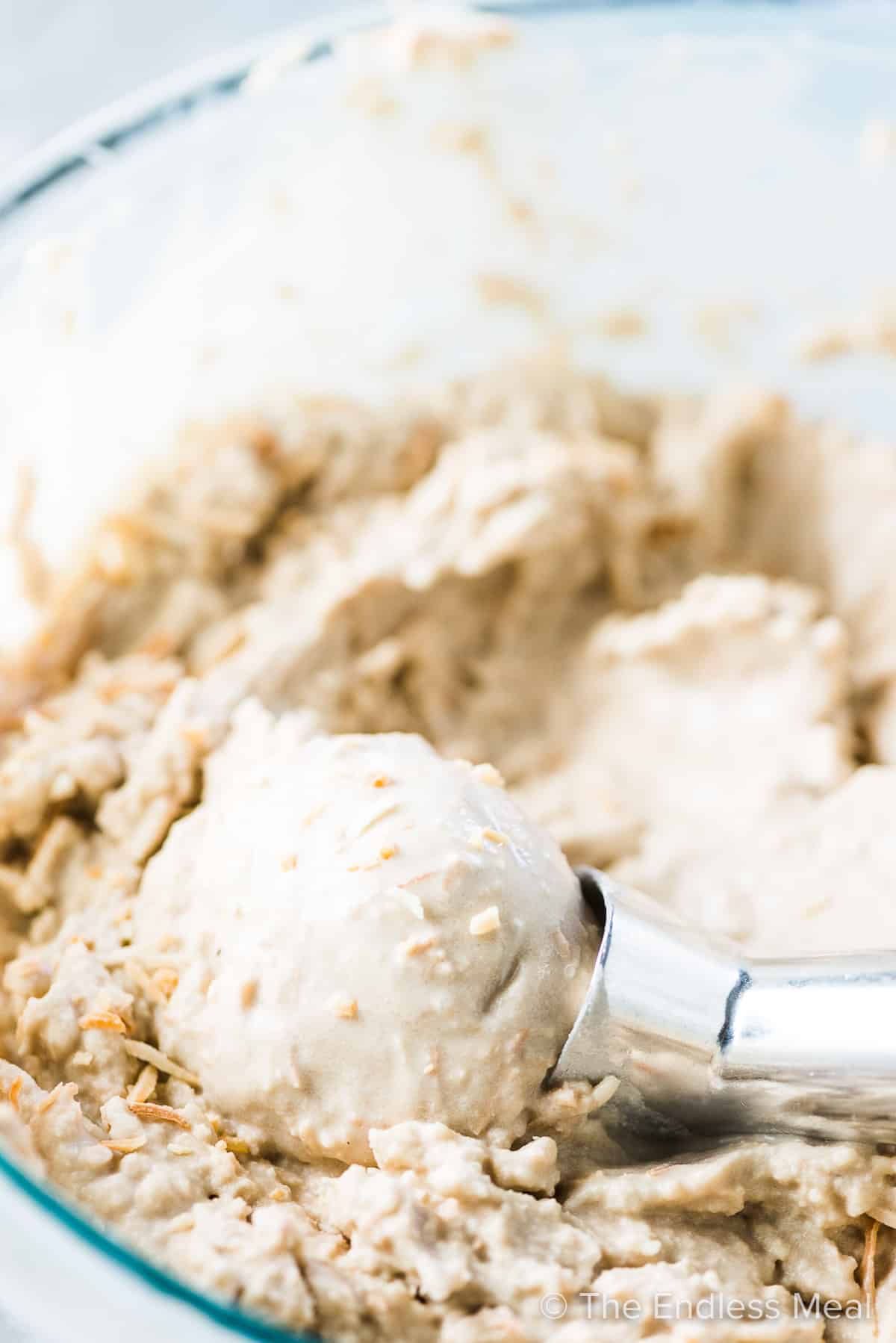 Toasted Coconut Ice Cream in a glass bowl with an ice cream scoop taking a scoop.