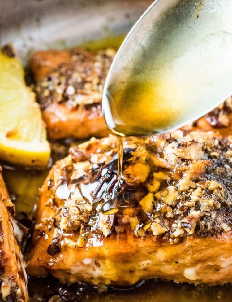 A spoon pouring the garlic maple glaze of the pecan crusted salmon.