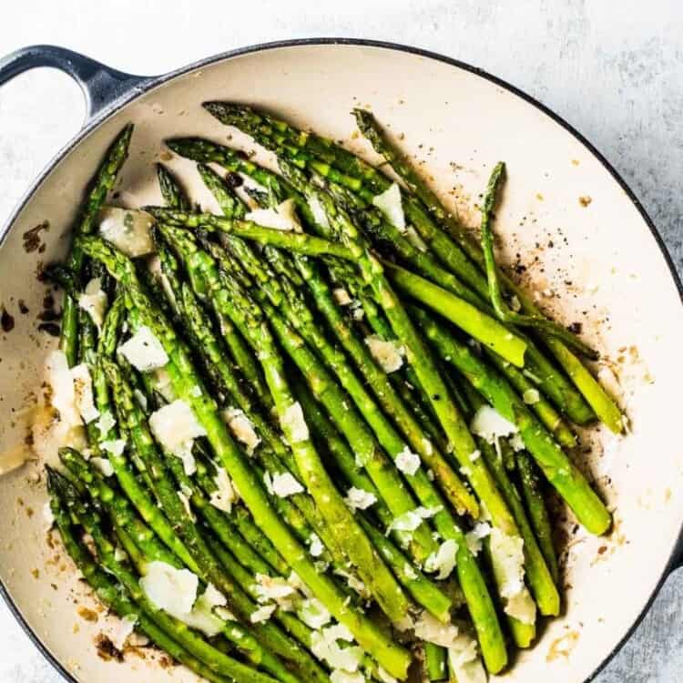 This sauteed asparagus recipe in a white pan with black handles on a white table.