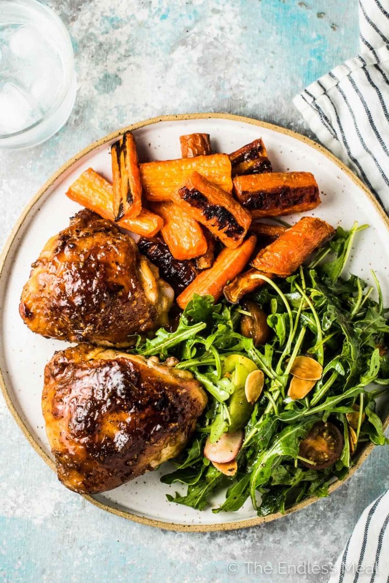 This honey garlic chicken recipe on a dinner plate with salad and roast carrots. 