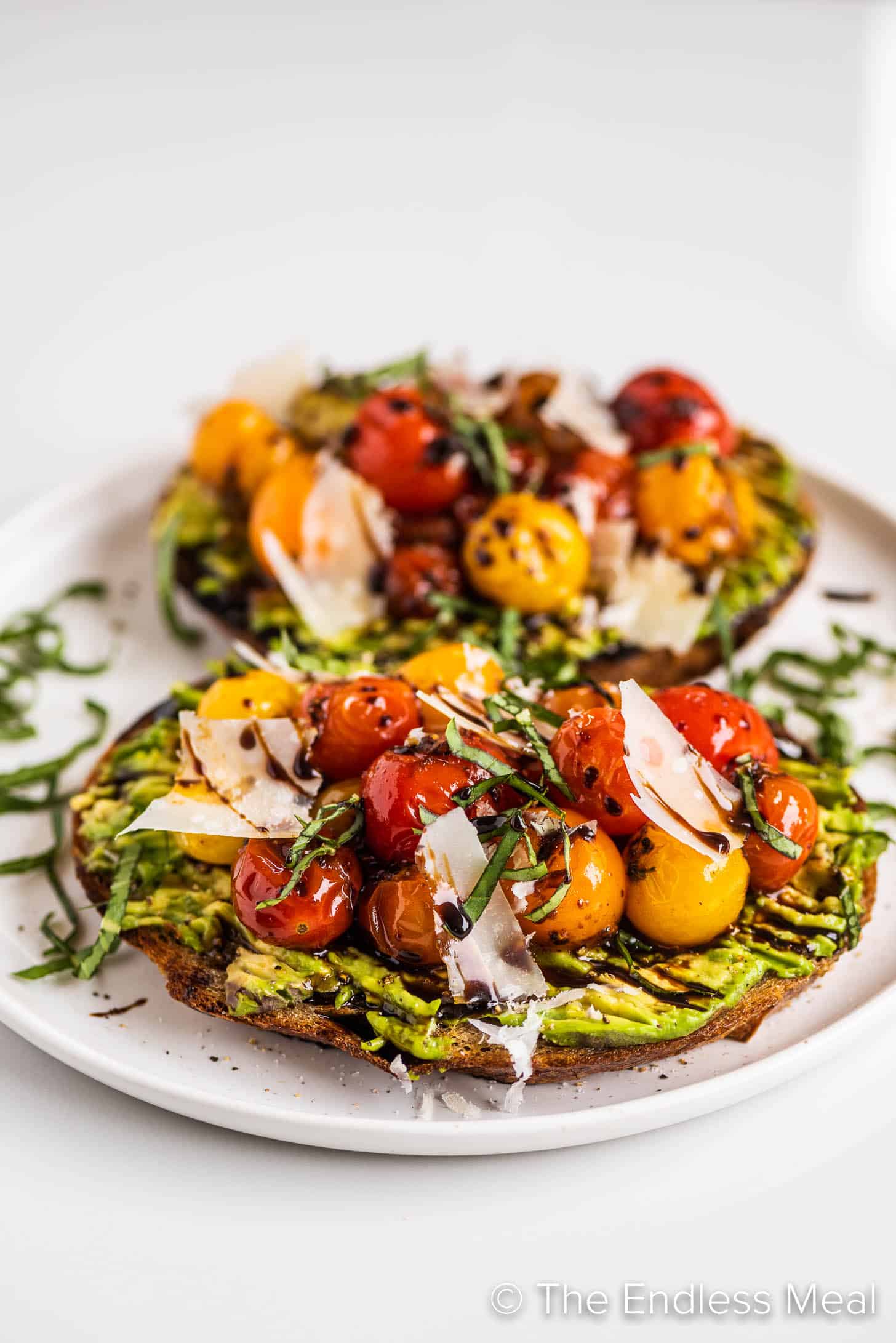 two slices of avocado toast with sauteed tomatoes on a plate