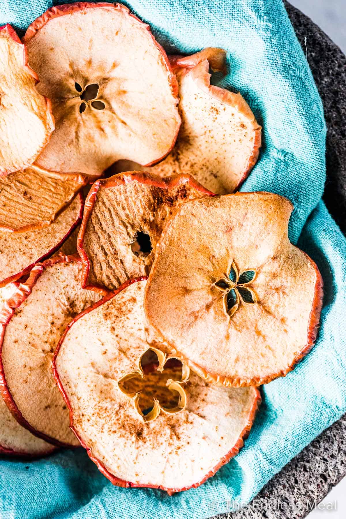 Baked apple chips in bowl lined with a blue cloth.