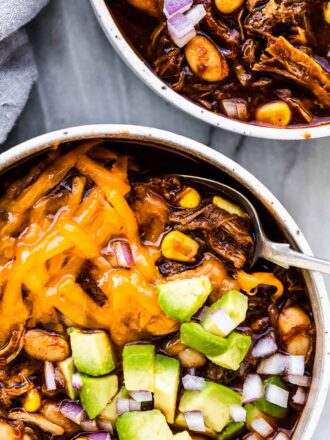 2 bowls of pulled pork chili topped with avocado and cheese.