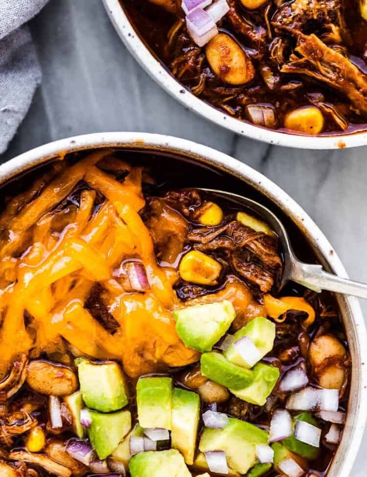 2 bowls of pulled pork chili topped with avocado and cheese.