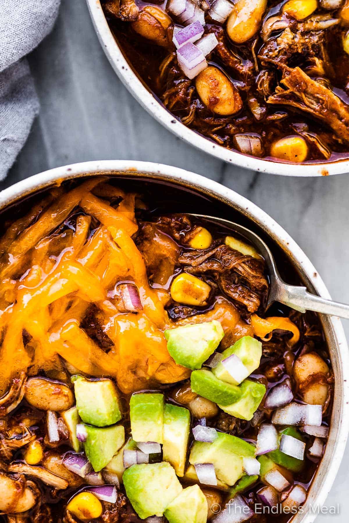 2 bowls of pulled pork chili topped with avocado and cheese. 
