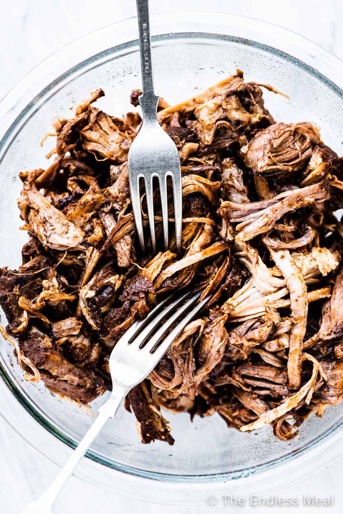 Pulled pork in a glass bowl with 2 forks. 