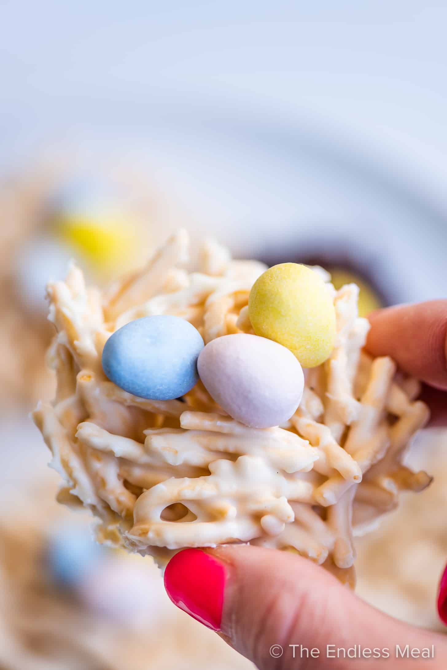 a hand holding a white chocolate bird's nest cookie filled with mini eggs
