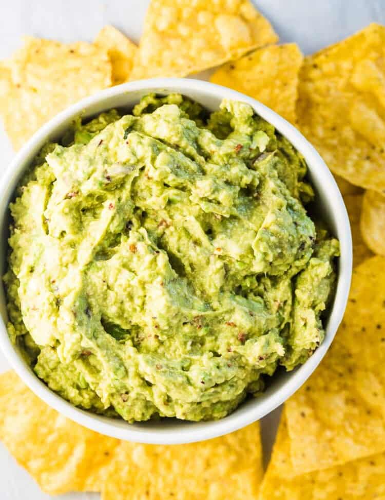Looking down on a bowl of chipotle guacamole dip surrounded by yellow corn chips.