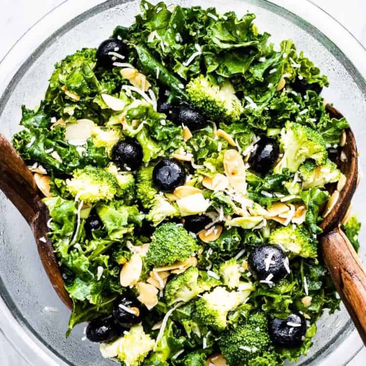 Broccoli Kale Salad with Blueberries and Coconut in a glass salad bowl with wooden tongs