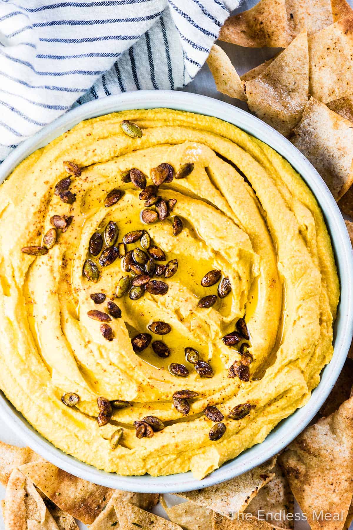 A blue bowl filled with pumpkin hummus with homemade pita chips surrounding it.
