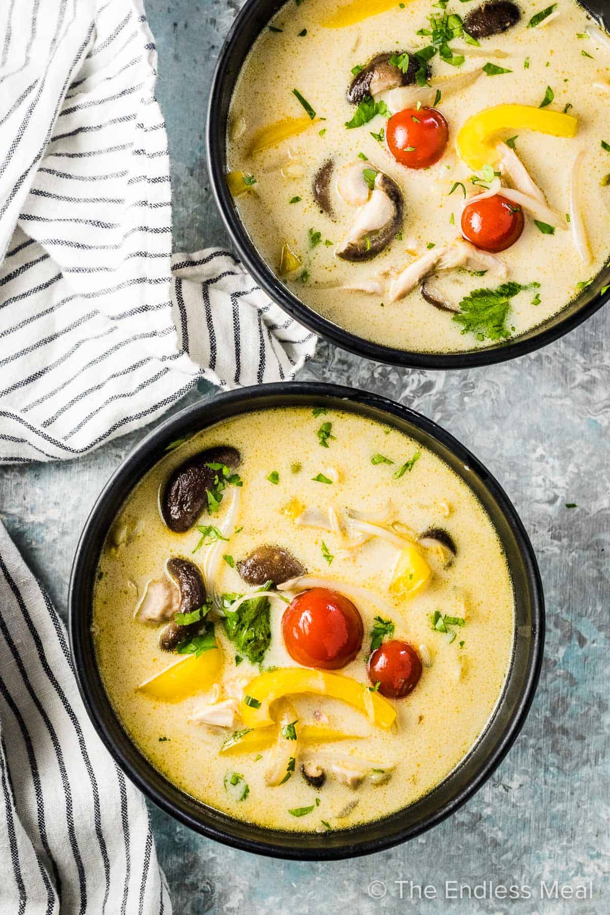 Two bowls of thai coconut curry soup in black bowls.