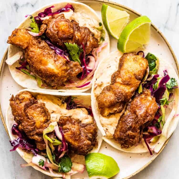 Looking down on three Beer Battered Fish Tacos on a white plate.