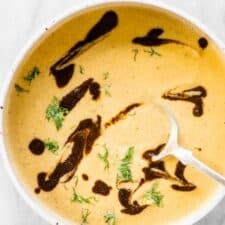 A bowl of roasted fennel black garlic soup with some black garlic drizzle on the top.