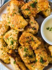 A plate of healthy baked chicken nuggets with a bowl of dipping sauce beside them.