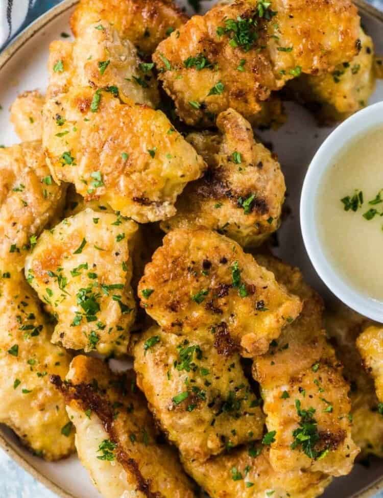 A plate of healthy baked chicken nuggets with a bowl of dipping sauce beside them.