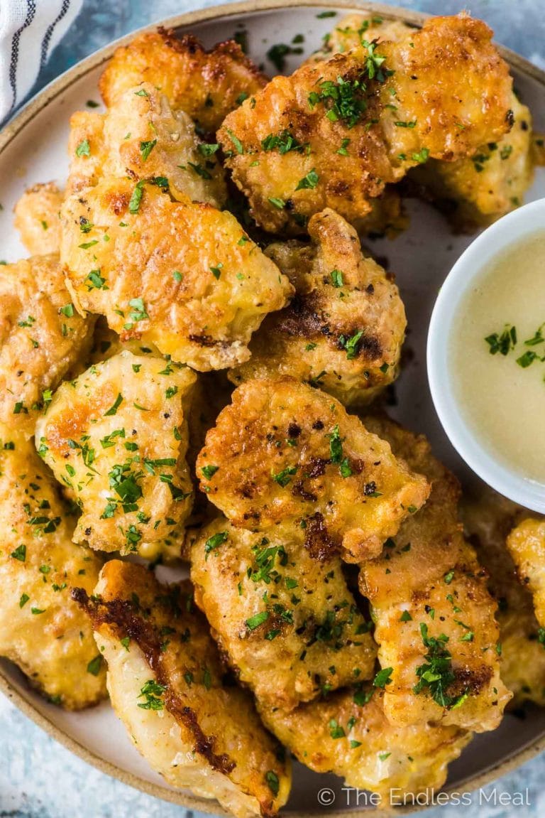 A plate of healthy baked chicken nuggets with a bowl of dipping sauce beside them. 