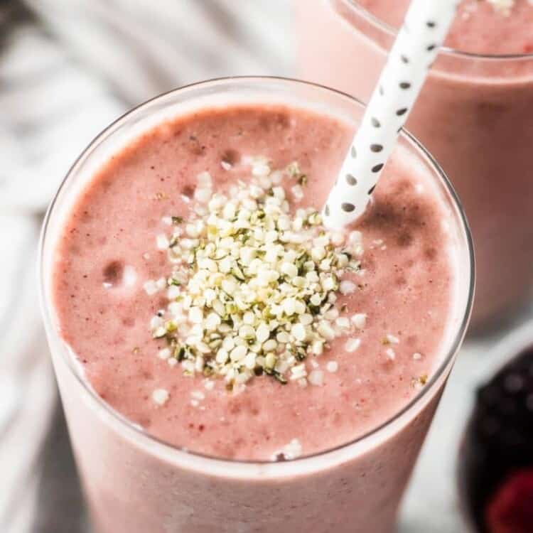 A pink almond butter smoothie with some hemp seeds sprinkled on top and a straw in the tall glass.