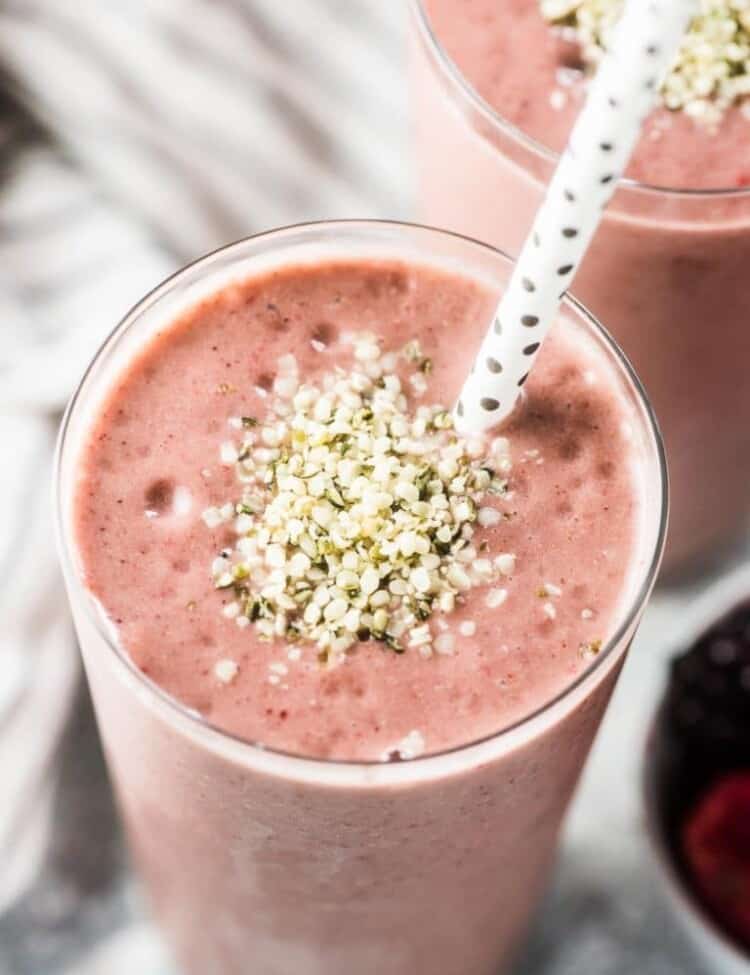 A pink almond butter smoothie with some hemp seeds sprinkled on top and a straw in the tall glass.