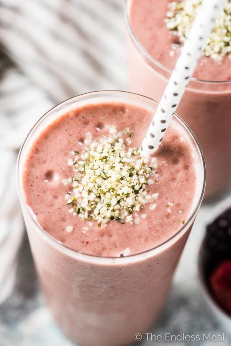 A pink almond butter smoothie with some hemp seeds sprinkled on top and a straw in the tall glass. 