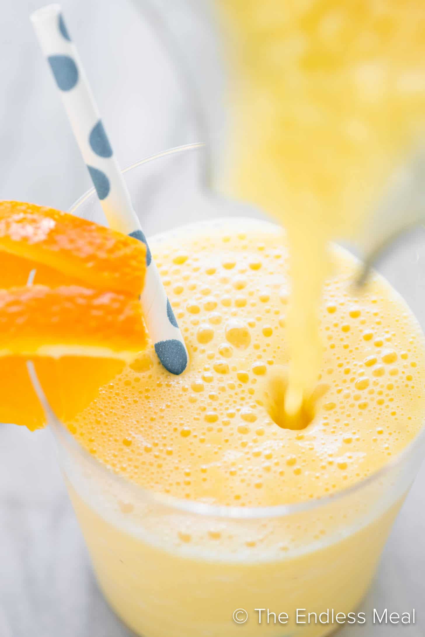 An orange creamsicle smoothie being poured into a cup.
