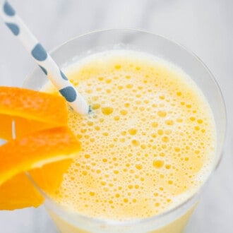 An orange creamsicle smoothie in a glass with a straw and orange slices.