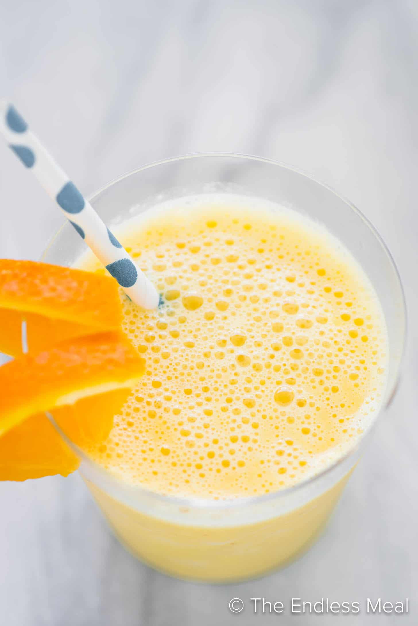 An orange creamsicle smoothie in a glass with a straw and orange slices.
