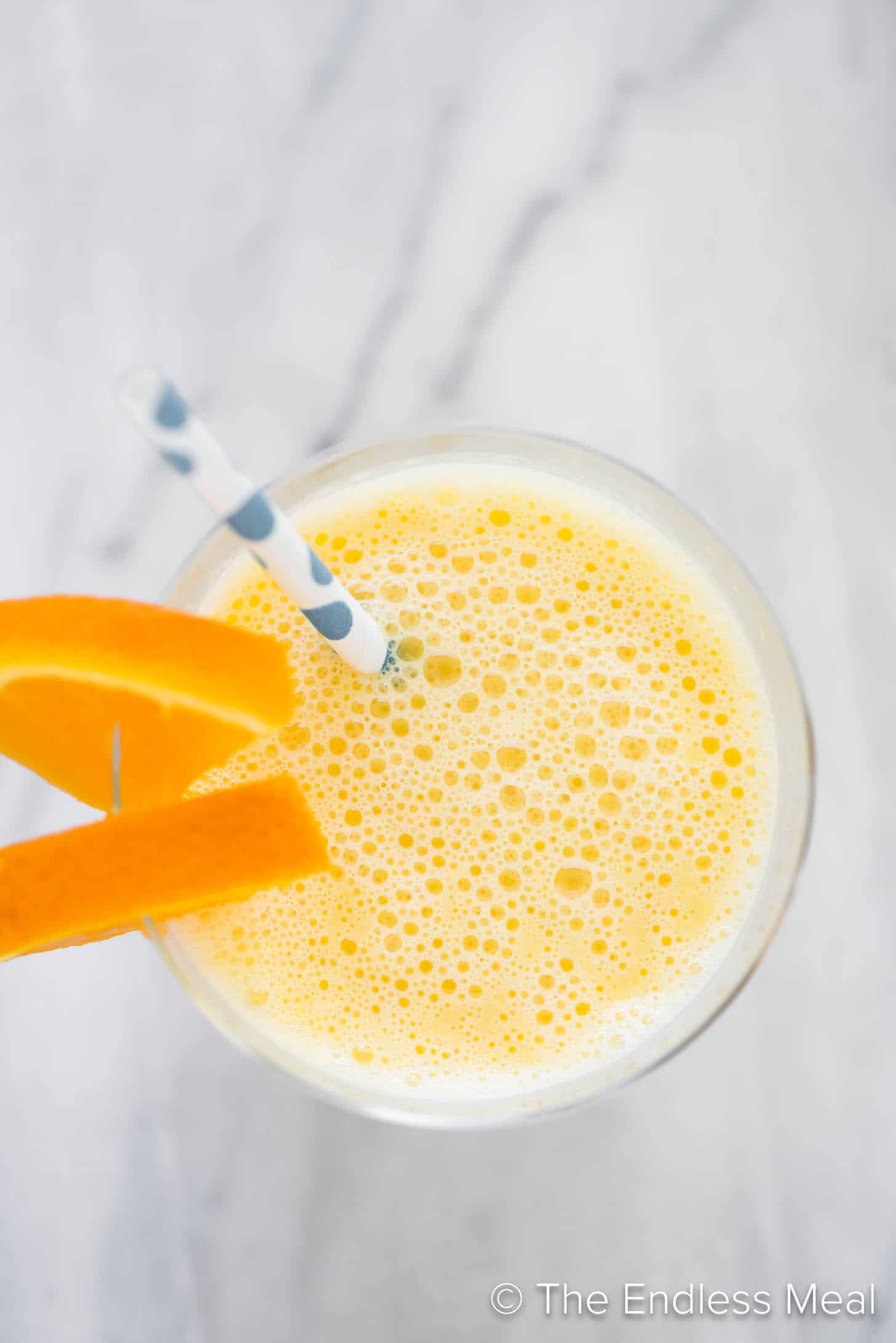 Looking down on an orange smoothie with a straw and orange slices.