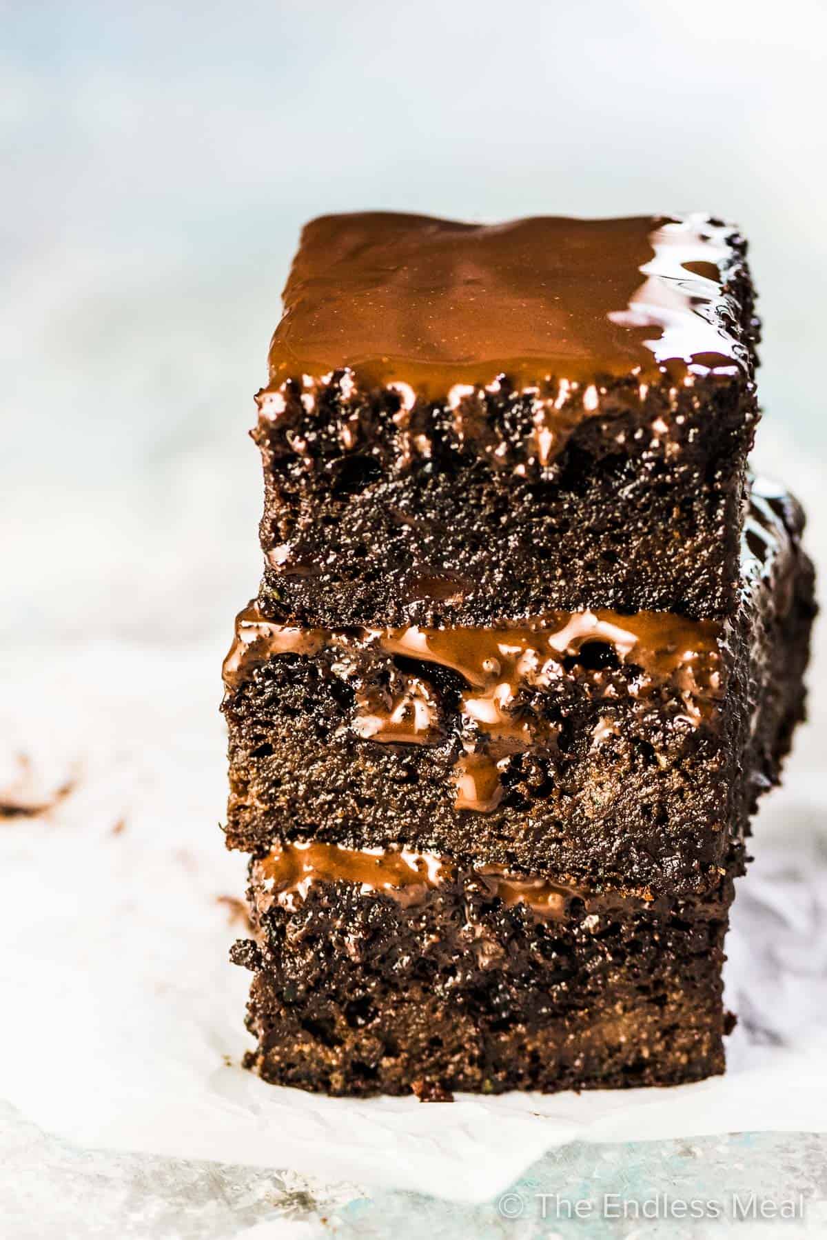 A stack of 3 zucchini paleo brownies with dripping chocolate glaze. 