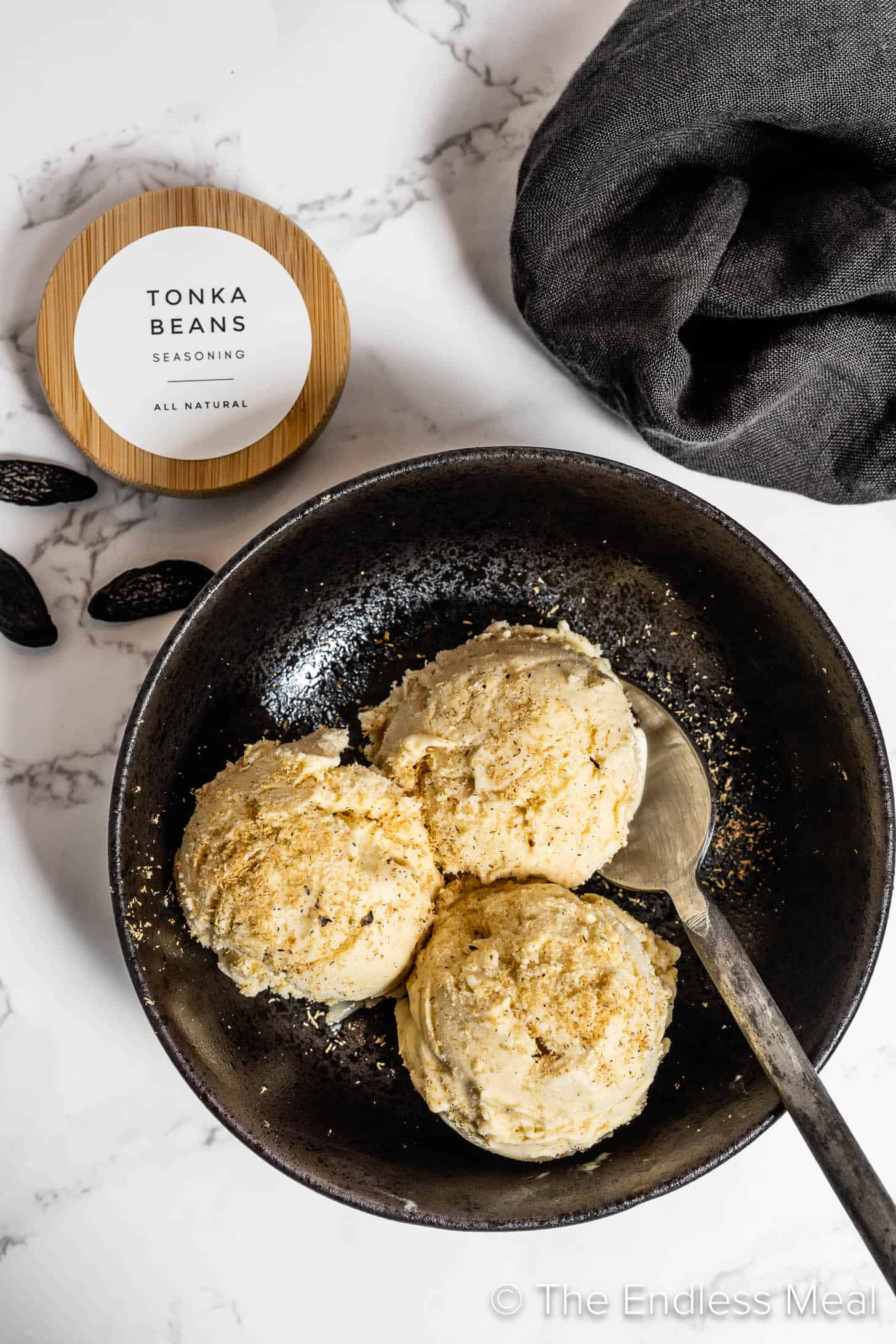 Tonka Bean Ice Cream in a dark bowl beside tonka beans