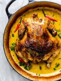 Whole coconut milk braised chicken in a braising pan with yellow curry sauce.