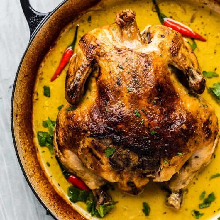 Whole coconut milk braised chicken in a braising pan with yellow curry sauce.