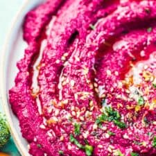 A close up of vibrant pink beet hummus with a little minced parsley, lemon zest, and sesame seeds on the top.