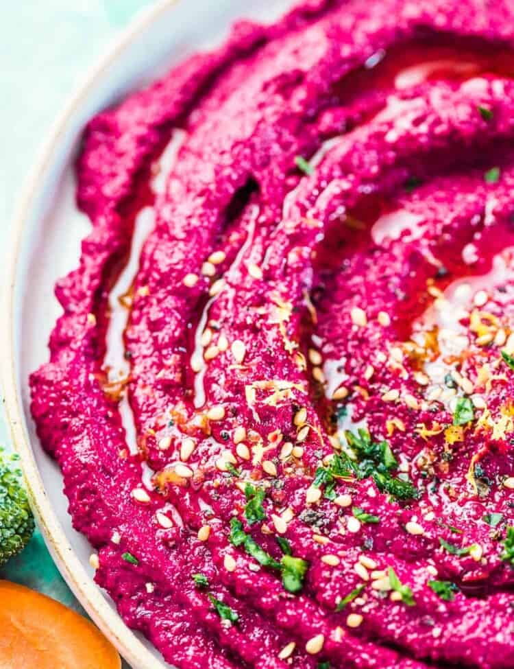 A close up of vibrant pink beet hummus with a little minced parsley, lemon zest, and sesame seeds on the top.