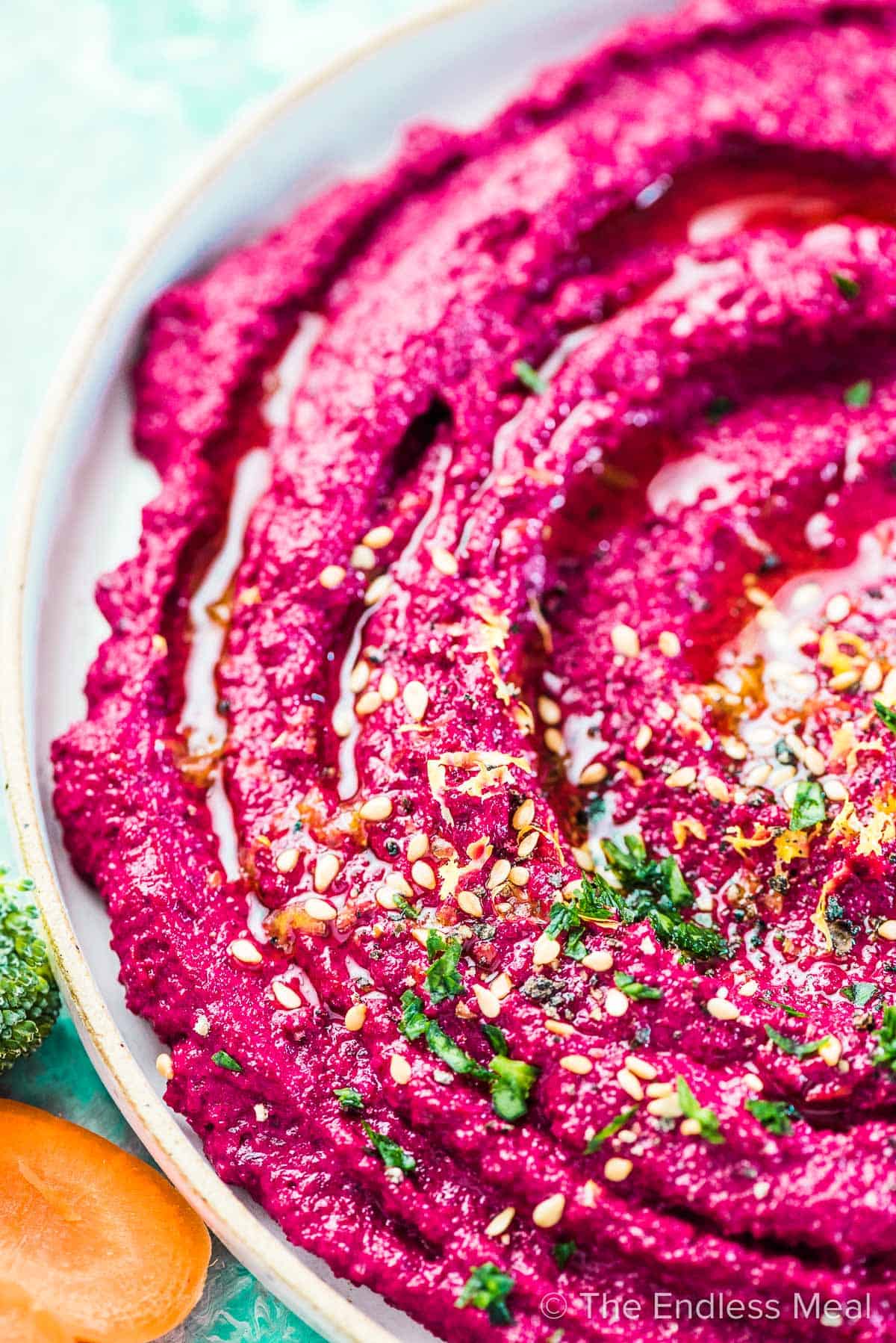 A close up of vibrant pink beet hummus with a little minced parsley, lemon zest, and sesame seeds on the top. 