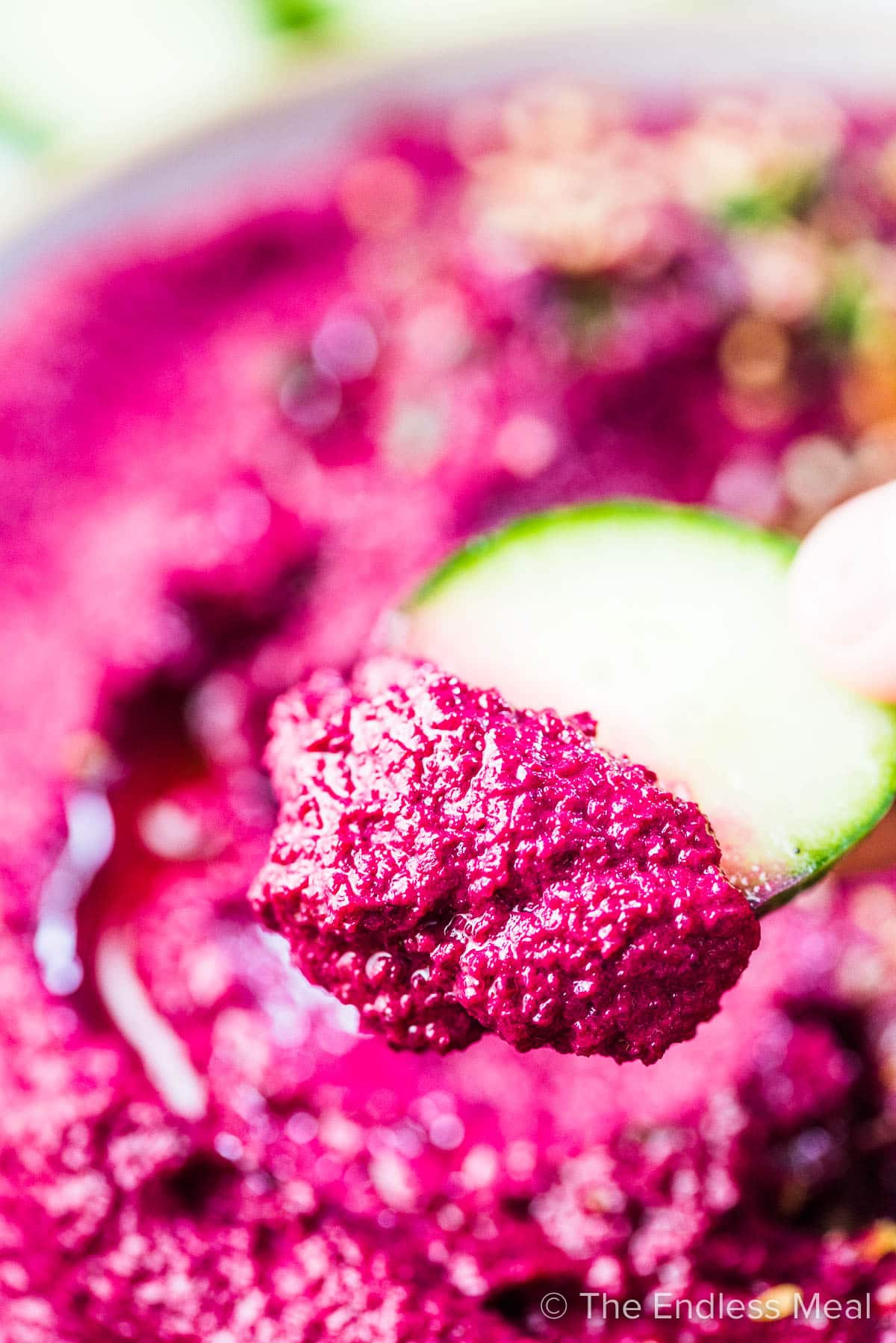 A cucumber slice taking a scoop of this beet hummus recipe.