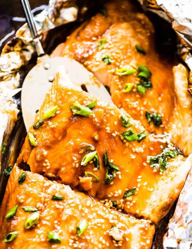 Glazed Asian salmon in foil on a baking sheet with a spatula lifting a piece of salmon.