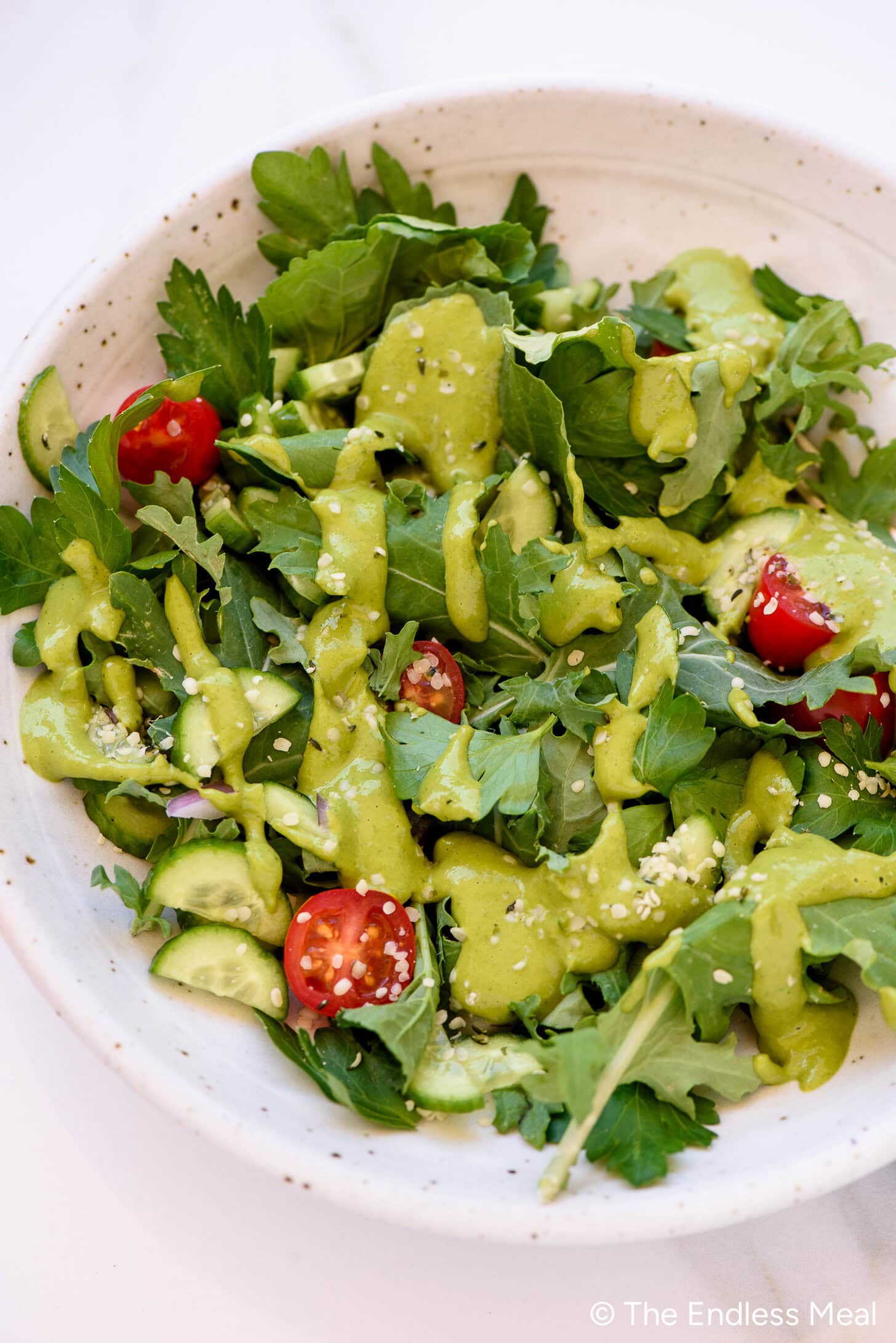 A bowl of leafy green salad with cherry tomatoes, cucumber slices, and a generous drizzle of green goddess dressing on top.