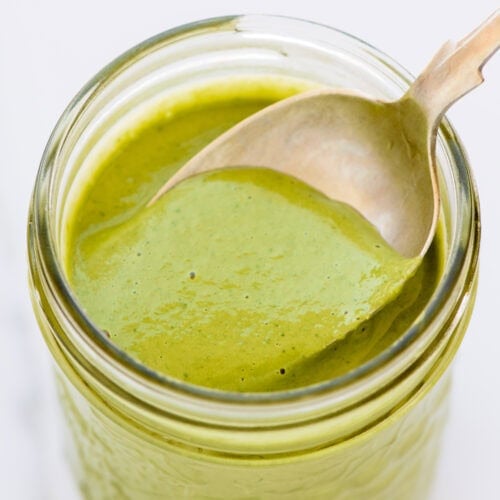 A jar filled with creamy green goddess dressing, with a spoon resting inside.