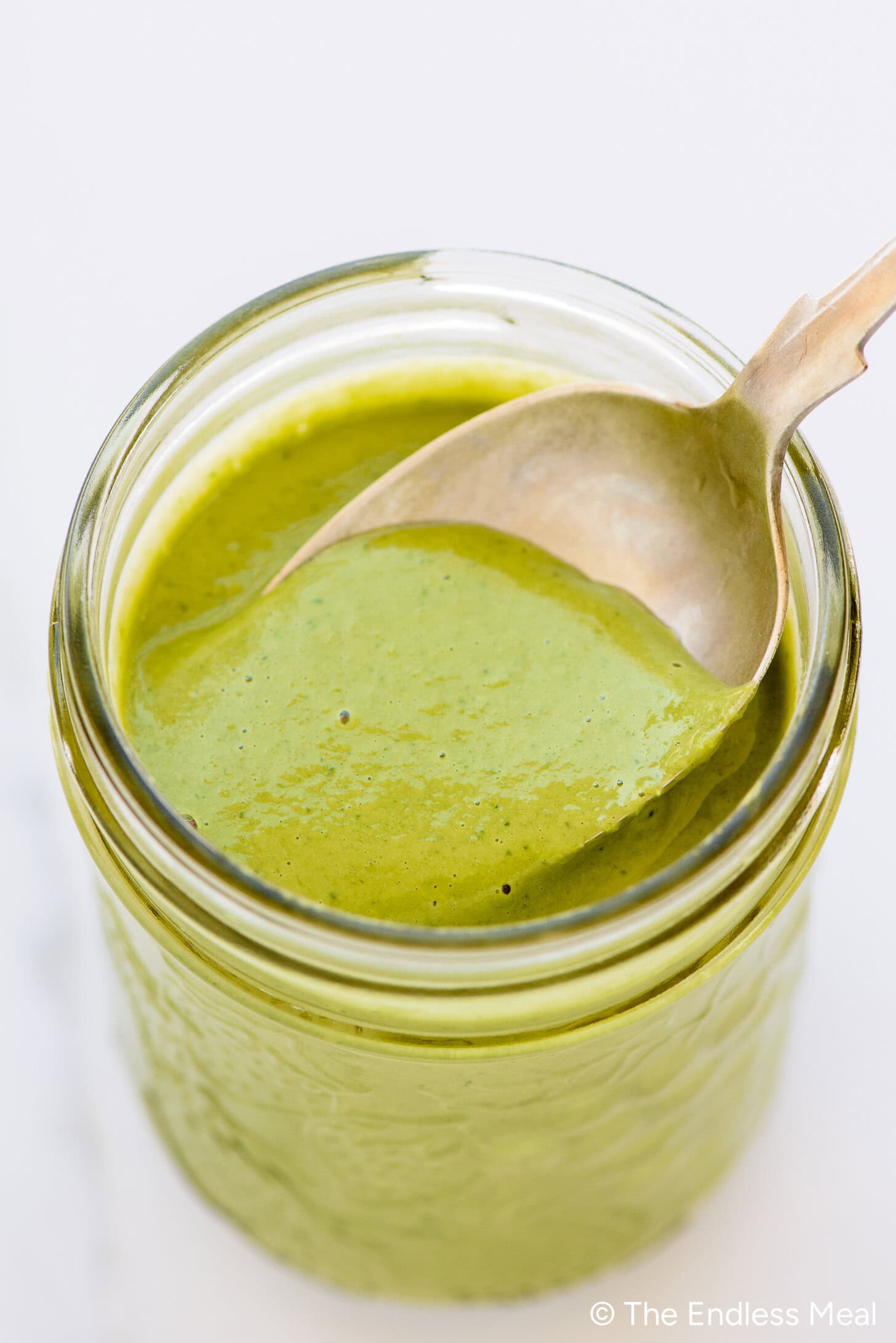 A jar filled with creamy green goddess dressing, with a spoon resting inside.