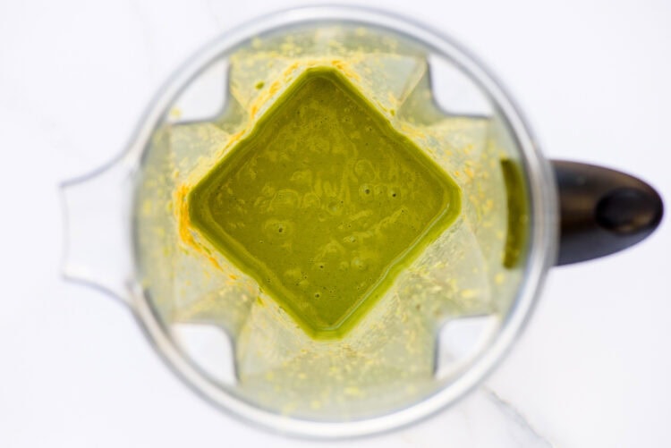 Overhead view of a blender containing a thick green liquid, possibly green goddess dressing or a smoothie, against a white background.