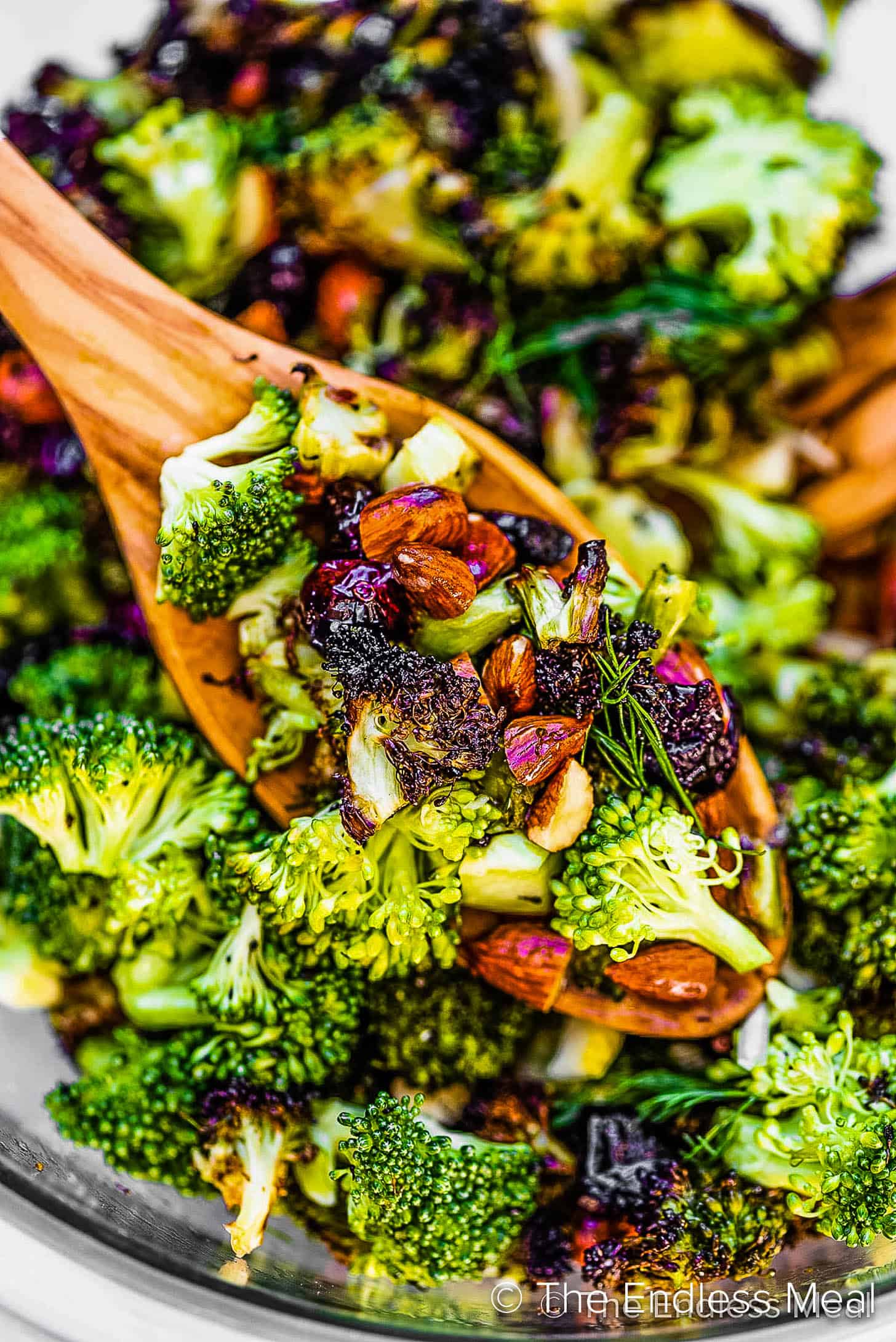 A scoop of roasted broccoli salad on a wooden spoon.