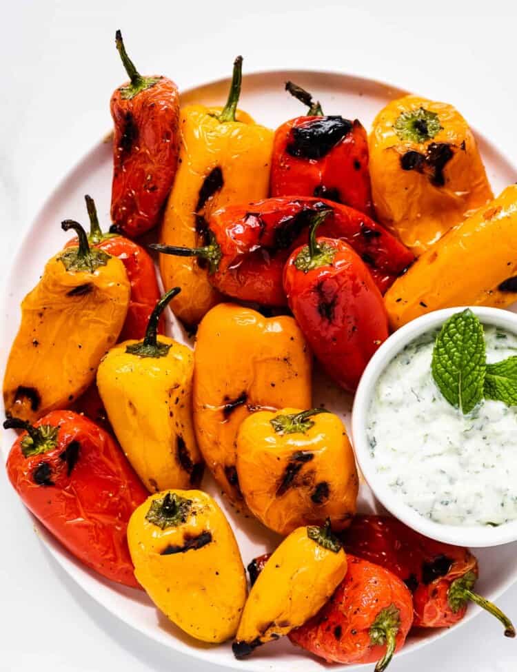 Grilled Mini Peppers on a serving plate with a side of mint tzatziki