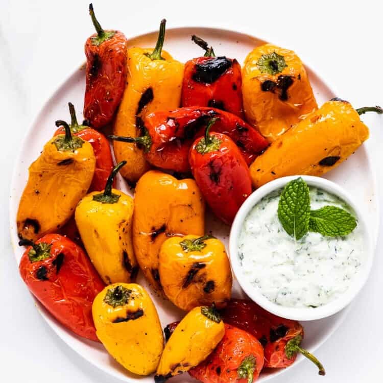 grilled mini peppers with mint tzatziki on a plate.