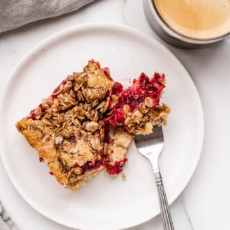 a slice of Cranberry Coffee Cake on a plate with a cup of coffee beside it.